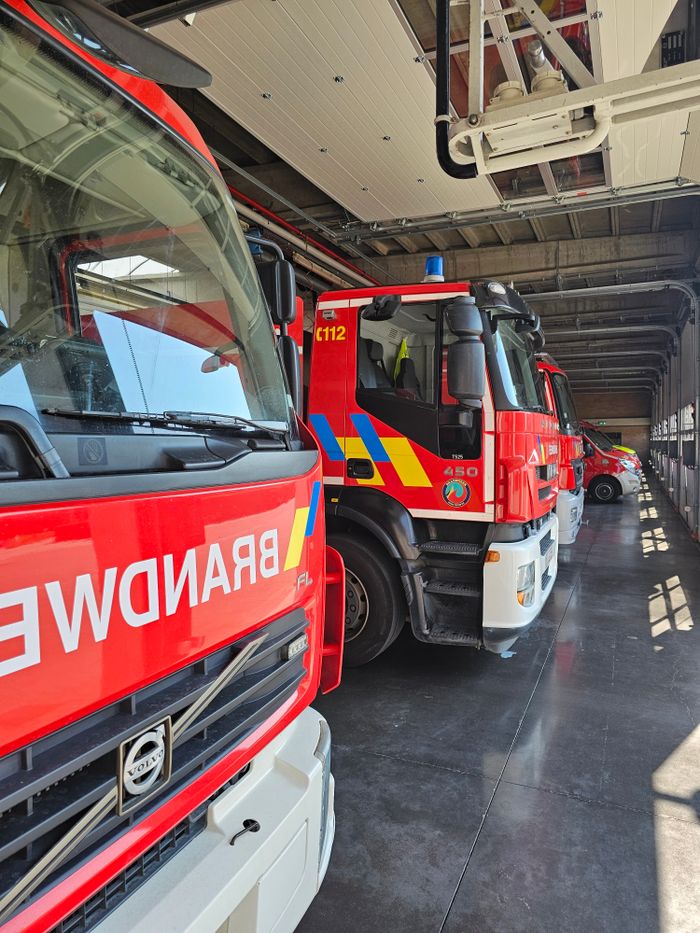 A row of bright red fire trucks parked inside a sunlit fire station, showcasing emergency readiness.